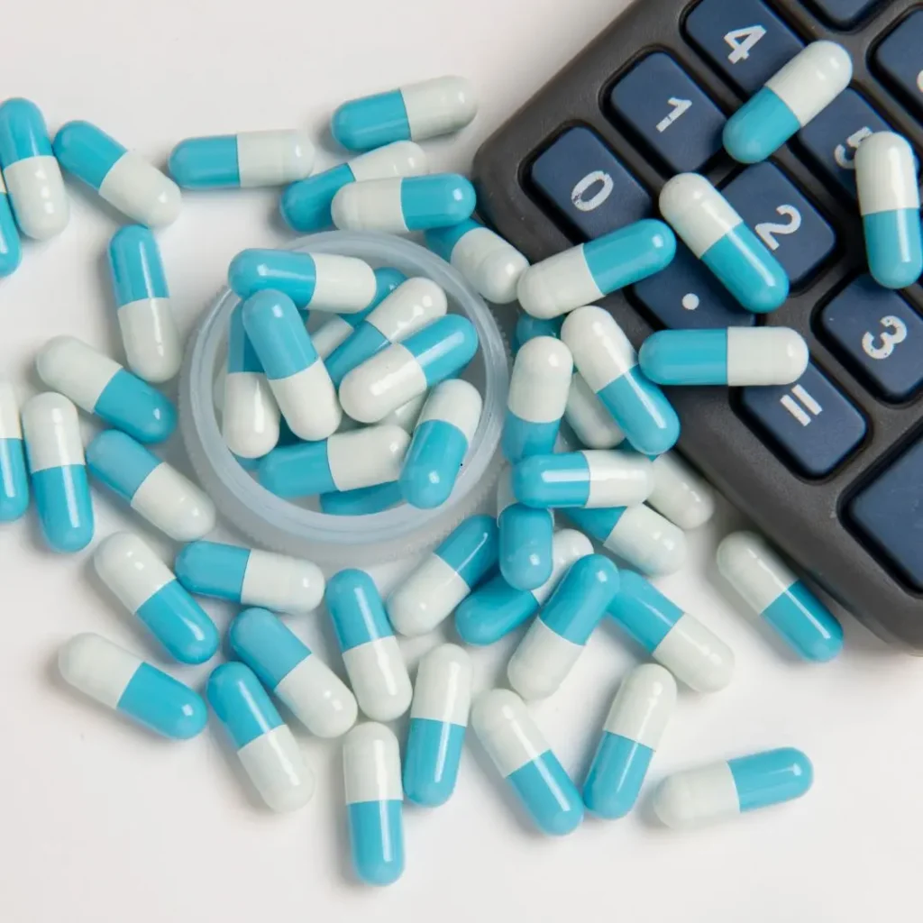 Cápsulas de medicamento espalhadas ao lado de uma calculadora
